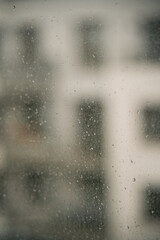 Rain droplets on the window glass. View from the window at the blurred street with buildings during bad weather.