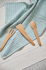 Kitchen utensils for cooking from natural and durable materials. A muslin towel of a beautiful light blue color, a wooden spatula, a spoon and a fork and a metal whisk. View from above.