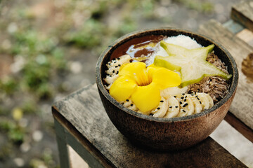 Smoothie bowl with tropical fruits carambola, bananas, decorated with a yellow tropical flower. View from above.