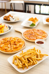 Buffet table scene of take out or delivery foods. Pizza, rice with fried chicken,French fries. Above view on a wood teble background