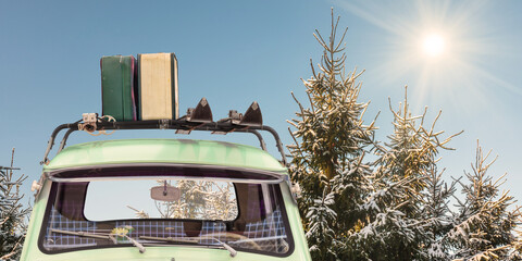 Vintage car with skis and luggage attached to a roof rack in front of snow covered fir trees with...