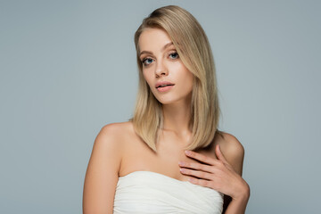 young blonde model with bare shoulders and natural makeup looking at camera isolated on grey.