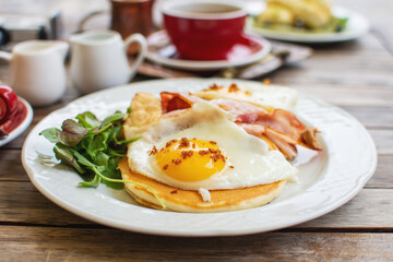 Tasty breakfast with pancakes, fried eggs and bacon on table