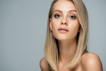 Fototapeta premium portrait of young blonde woman with blue eyes and natural makeup looking at camera isolated on grey.