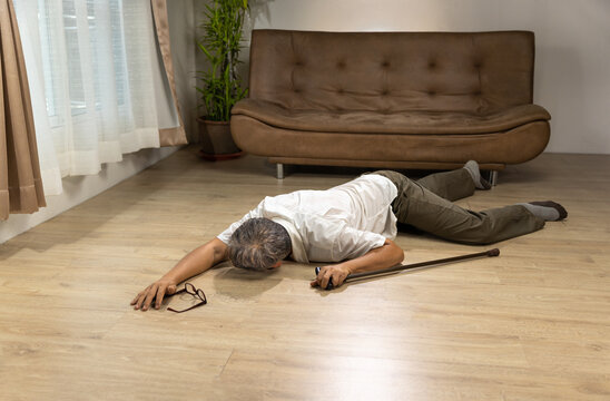 Asian senior man falling down and lying on the floor while walk with walking stick at home.