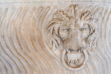 Lion head holding a knocker carved in marble wall