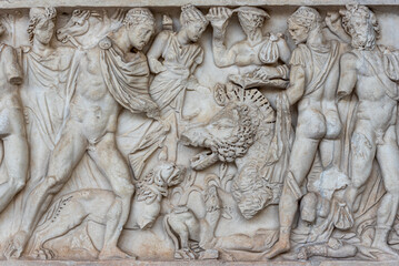 Fototapeta na wymiar Sculptures carved in marble wall showing a group of naked men in a hunt in ancient Rome