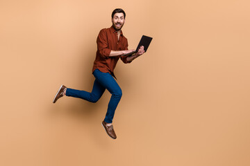Fototapeta na wymiar Full length profile portrait of energetic excited guy hold use netbook jump run empty space isolated on beige color background