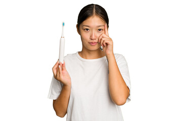 Young Asian woman holding an electric toothbrush isolated on green chroma background pointing temple with finger, thinking, focused on a task.