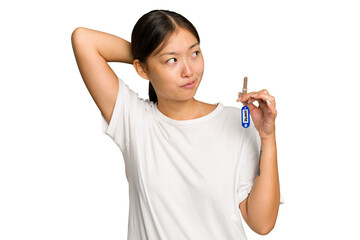 Young asian woman holding home keys isolated on green chroma background touching back of head, thinking and making a choice.