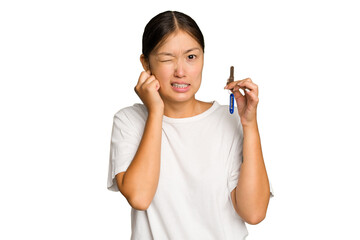 Young asian woman holding home keys isolated on green chroma background covering ears with hands.
