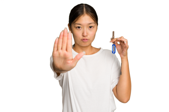 Young asian woman holding home keys isolated on green chroma background standing with outstretched hand showing stop sign, preventing you.