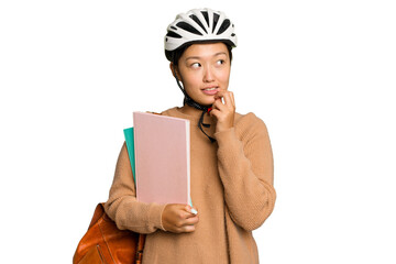 Young student asian woman wearing a bike helmet isolated on green chroma background relaxed thinking about something looking at a copy space.