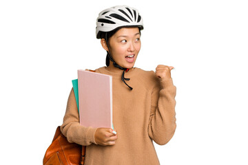 Young student asian woman wearing a bike helmet isolated on green chroma background points with thumb finger away, laughing and carefree.