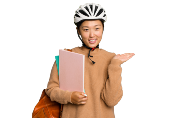 Young student asian woman wearing a bike helmet isolated on green chroma background showing a copy space on a palm and holding another hand on waist.