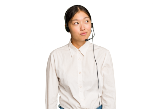 Telemarketer asian woman working with a headset isolated on green chroma background dreaming of achieving goals and purposes