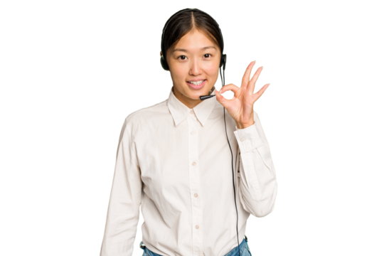 Telemarketer asian woman working with a headset isolated on green chroma background cheerful and confident showing ok gesture.