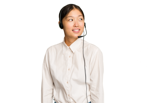Telemarketer asian woman working with a headset isolated on green chroma background looks aside smiling, cheerful and pleasant.