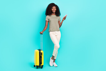 Full size portrait of cheerful nice girl hand hold telephone suitcase isolated on shiny turquoise color background