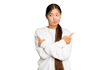 Young Asian woman isolated on green chroma background points sideways, is trying to choose between two options.