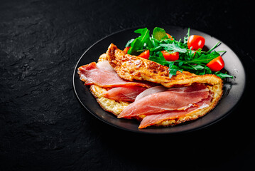 omelette with prosciutto and salad on black plate on Dark grey black slate background