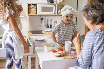 Mother and cute baby boy and girl cooking food at childish kitchen playing chef educational playthings