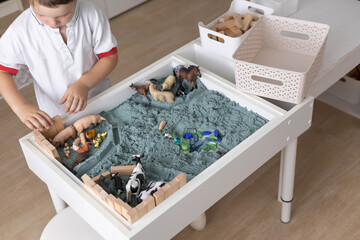Cute baby boy playing sensory box kinetic sand table with farm animals