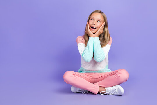 Full length photo of astonished girl sit arm touch face look empty space unexpected unbelievable offer isolated on purple color background