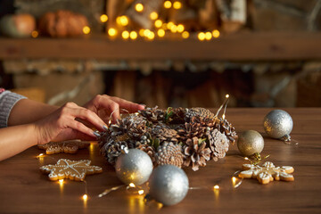 woman holds a Christmas wreath of cones in her hands, on a wooden table. Christmas wreath making