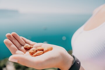 Young milky almond nuts in womans hand. A young caucasian woman eating fresh almond after morning fitness yoga near sea. Only hands are visibly. Healthy vegan food.