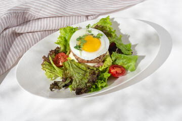 Croque madam sandwich with cheese, ham and egg on a plate on a light table. Hearty homemade breakfast.