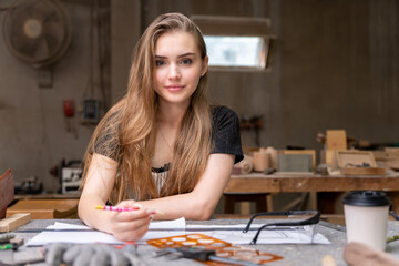 Fototapeta premium Portrait of a female carpenter drawing on paper for designing and building furniture in a furniture factory. with modern tools