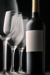 An elegant bottle of red wine with an empty label and three beautiful glasses in close-up. Graphic minimalistic still life on a black background.