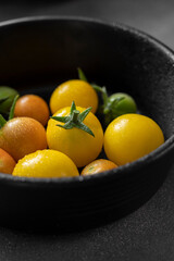 Yellow, small cherry tomatoes in black bowl. LIfestyle moody vegetables photo