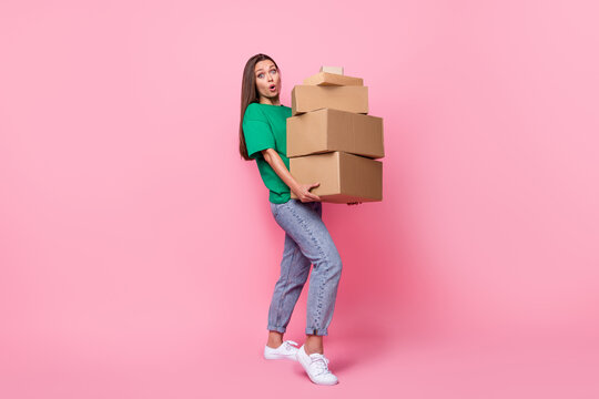 Full size photo of gorgeous nice cute girl with long hairstyle wear green t-shirt jeans hold heavy boxes isolated on pink color background