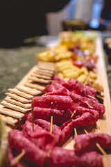 Big wooden board with salami, crackers, mini corns, charcuterie, variety of cheeses, cherry tomatoes, nuts, etc