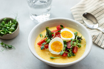 polenta, corn porridge with fresh vegetables, microgreens and eggs on gray table. Delicious healthy breakfast. close-up