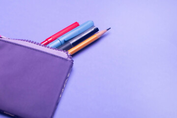 Fashionable violet pencil case with multicolored felt-tip pens, pencils and pens on lilac background.