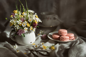 Obraz na płótnie Canvas Wild flowers in white mug, sweets und cup of tea on grey background.Rustic template for postcard.Women's day, Mothers Day concept.Imitation of an old photo.