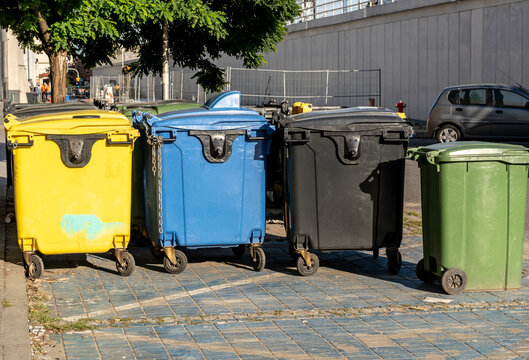 Black, blue, yellow, green garbage containers in city.  Separate waste, preserve the environment concept. Segregate waste, sorting garbage bins. Colored trash cans with paper, plastic, glass, organic