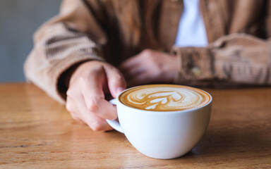 Closeup image of a woman holding a cup of hot latte coffee on wooden table