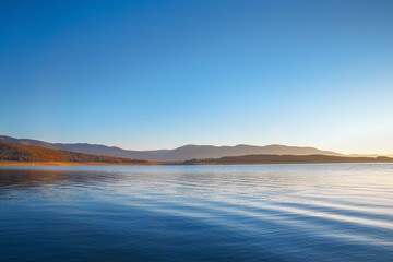 Beautiful sunrise over lake scenery in blue and yellow colors. Clear blue sky over calm lake during...