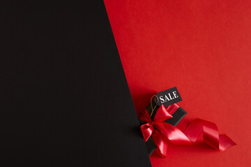 Black Friday sale concept with black gift box and text on sale tag on red and black background. Minimal flat lay with copy space.