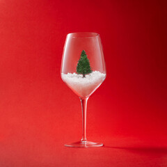 Christmas concept. Creative layout made of сhampagne glass with christmas tree and snow on red background. Minimal New year party idea.