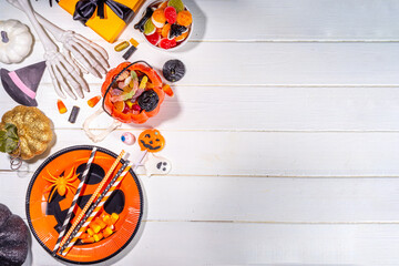 Halloween sweets and snacks table. Set of Halloween dinner party foods, candy, snacks, with holiday costume decorations, pumpkin buckets, wooden background top view copy space