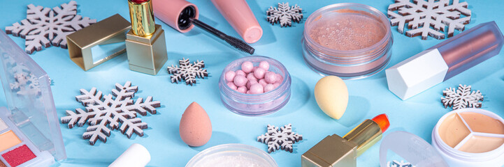 Winter make up set on light blue background, with artificial snowflakes and Christmas tree branches. Various makeup professional cosmetics - shadows, lipstick, mascara, blush. Christmas beauty sale