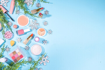 Winter make up set on light blue background, with artificial snowflakes and Christmas tree branches. Various makeup professional cosmetics - shadows, lipstick, mascara, blush. Christmas beauty sale