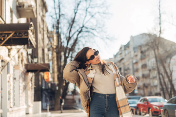 Portrait of beautiful hispanic woman in sunglasses and jacket posing at camera on sunny street in...