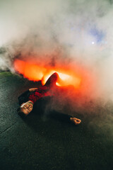 Obraz premium Adult man lying on the ground at night in the smoke near a burning car got into a car accident. Vertical