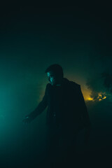 Night portrait of a man in a suit standing at night on a foggy street in the green light and looking away. Vertical